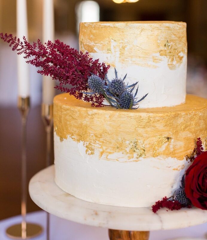 Wedding cake covered in gold leaf with maroon and purple flowers