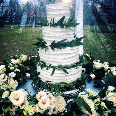4 tier wedding cake with greenery surrounded by flowers