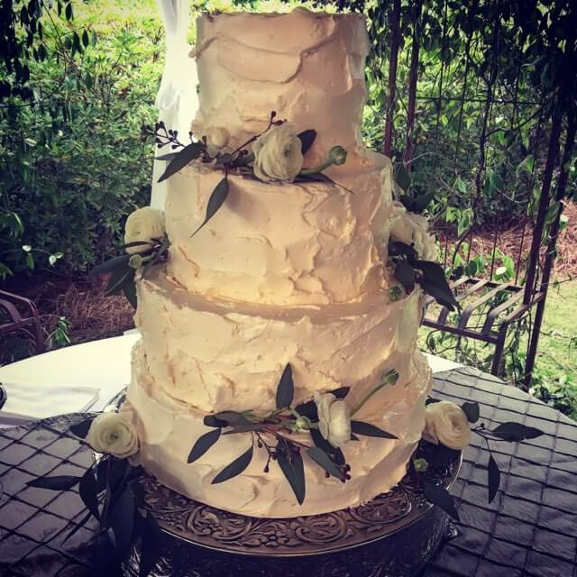 Wedding cake decorated with textured buttercream, white roses, and greenery