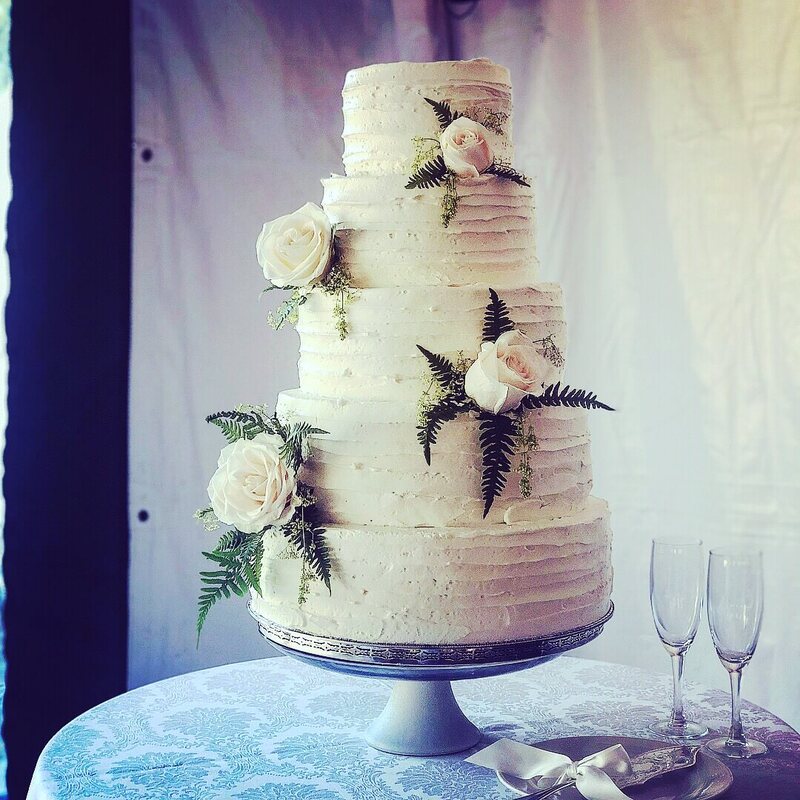 Elegant wedding cake with rippled icing and covered in flowers and greenery